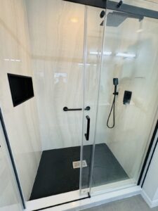 Walk-in shower with a black shower base, glass sliding door, large-format wall panels and a recessed niche